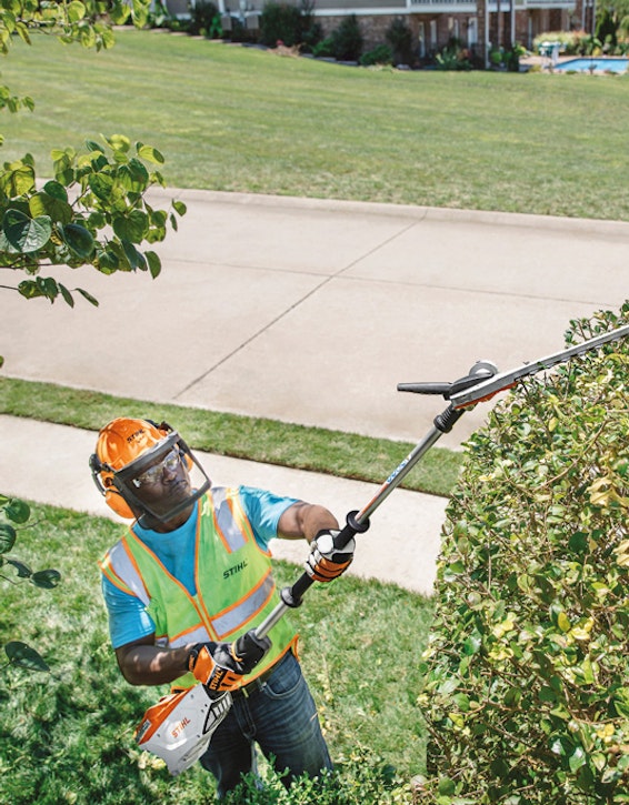 Man trimming hedges with extended reach hedge trimmer