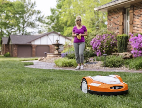Robotic mowing grass while woman looks at phone in the background
