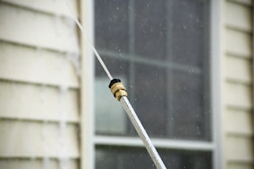 close up of black pressure washer nozzle spraying house siding
