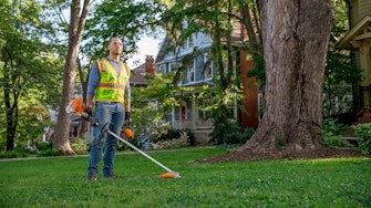 Professional landscaper holding an FS 91 R Trimmer surveying a trimmed residential yard.