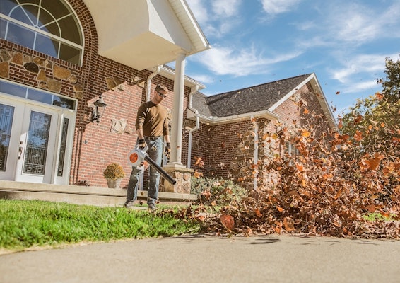 Man using the STIHL BG 50 Blower to blow a large pile of leaves off of the sidewalk.