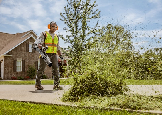 Professional landscaper using a BR 700 x backpack blower to blow grass off the sidewalk.