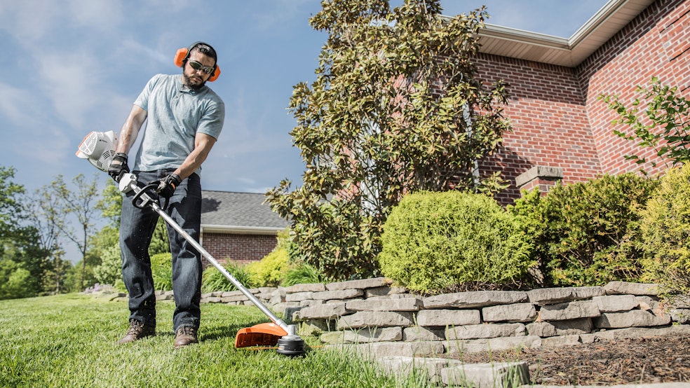 Man using FS 56 RC-E Trimmer near a flower bed at his home.