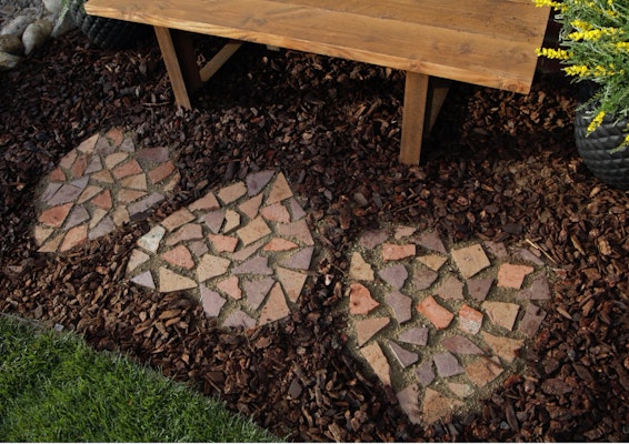 A heart shaped brick mosaic surrounded by mulch in a garden. 