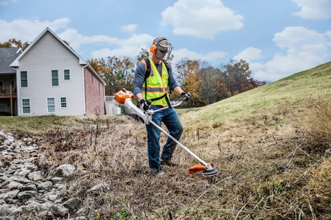 Profession landscaper using the STIHL FS 360 C-EM in a ditch near houses.