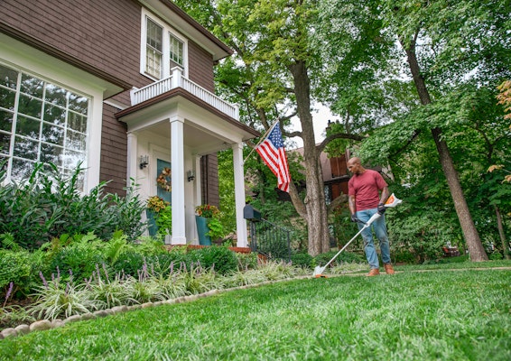 Man using FSA57 to trim grass with American flag behind 
