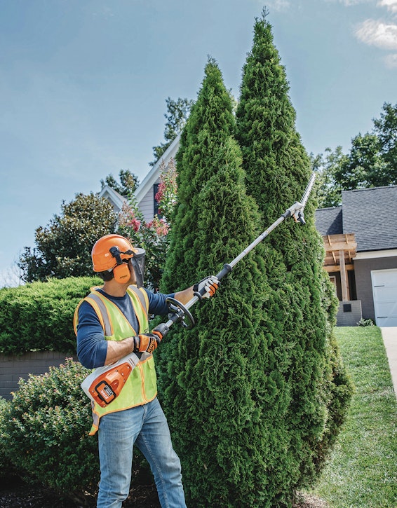 Professional landscaper using the HLA 135 to trim tall hedges. 