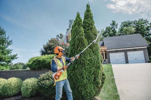 Professional landscaper using the HLA 135 to trim tall hedges. 