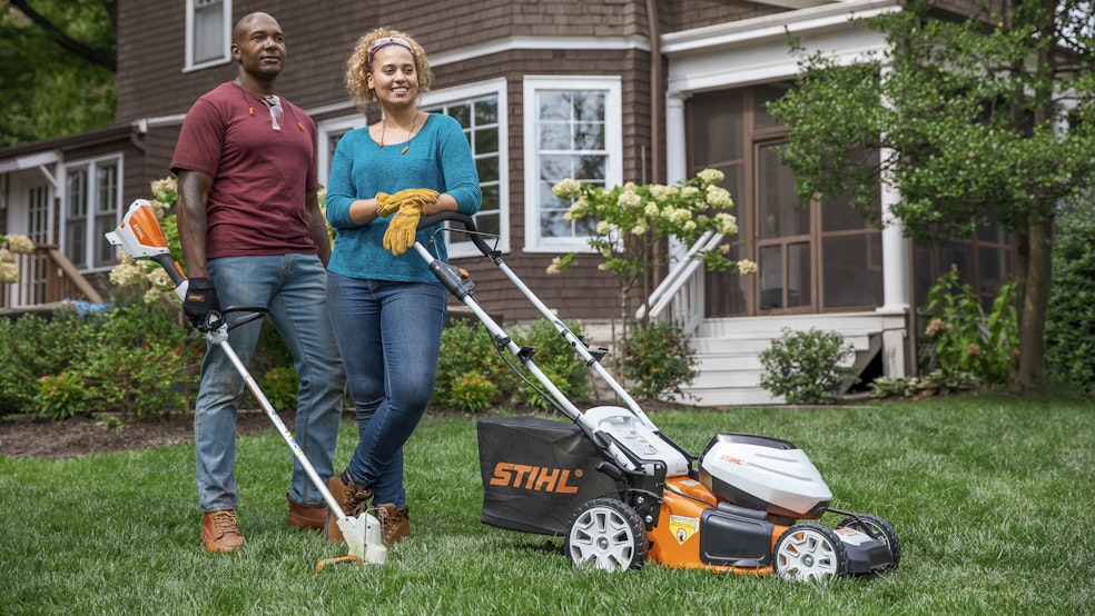 Happy couple standing in yard with mower and trimmer