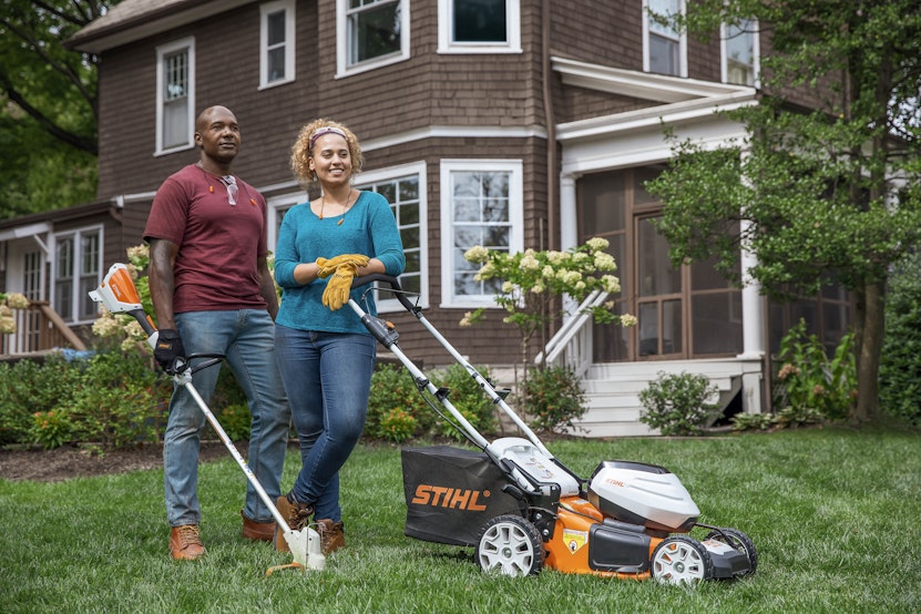 Happy couple standing in yard with mower and trimmer
