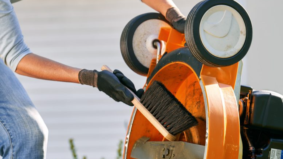 Person using brush to clean the underside of a lawn mower