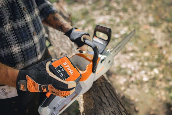 Man holding STIHL AK 30 battery and STIHL battery-powered chainsaw