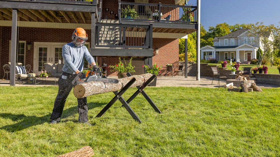 Man using STIHL MS 250 chainsaw to cut wood in backyard